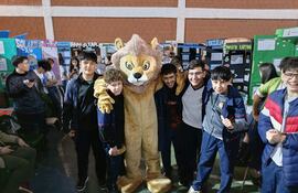 Grupo de seis jóvenes sonrientes en uniformes escolares, rodeando un disfraz de león en un ambiente escolar.