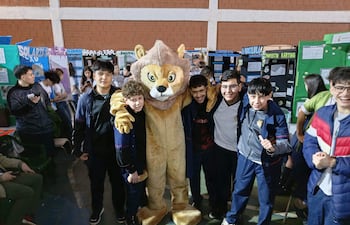 Grupo de seis jóvenes sonrientes en uniformes escolares, rodeando un disfraz de león en un ambiente escolar.