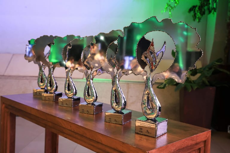 Trofeos estilizados en mesa de madera con iluminación festiva, representando hojas y ramas, en un evento de premiación.