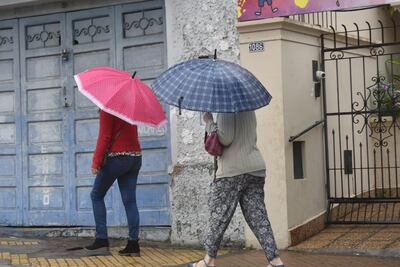 Dos mujeres con paraguas caminan bajo la lluvia en una calle de Asunción.