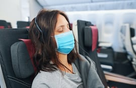 Una mujer con mascarilla viaja en un avión.