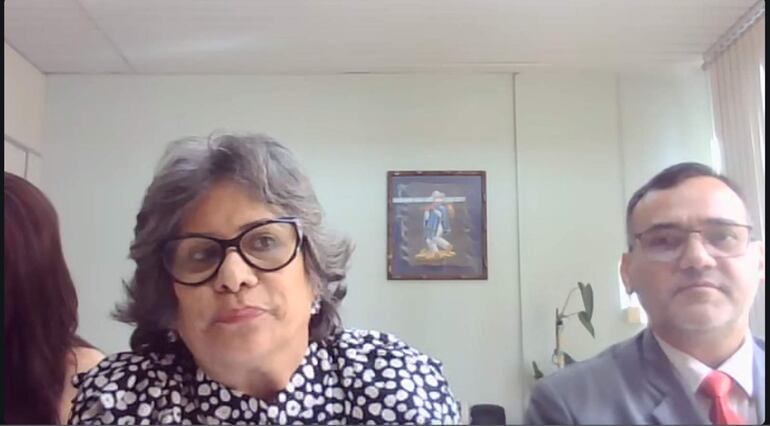 Laura Ocampo con cabello rizado y gafas habla, mientras Fabián Weisensee la escucha atentamente, en un entorno formal.