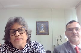 Laura Ocampo con cabello rizado y gafas habla, mientras Fabián Weisensee la escucha atentamente, en un entorno formal.
