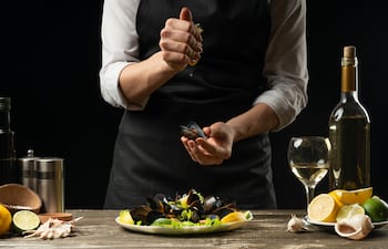 Chef rociando jugo de limón sobre mejillones.