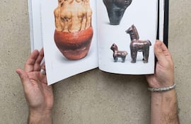 Manos sosteniendo un libro abierto con figuras de cerámica en sus páginas, sin personas visibles.