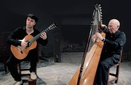 Lorenzo Paris, hombre mayor con arpa, e Ismael Rosillo, joven con guitarra, en un recital en lugar cálido y acogedor.