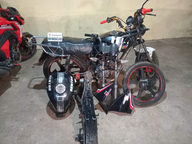 Motocicleta desarmada en taller, etiquetada como evidencia policial, con desgaste evidente y piezas faltantes.