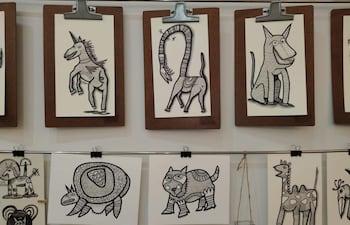 Varias ilustraciones de animales como un unicornio y una tortuga, enmarcadas, expuestas en paneles sobre soporte marrón.