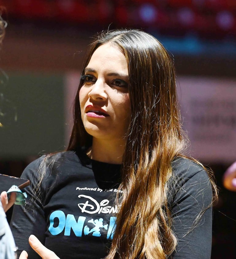 Mujer con cabello largo y castaño, vestida con camiseta negra de Disney On Ice, participa en una conversación animada.