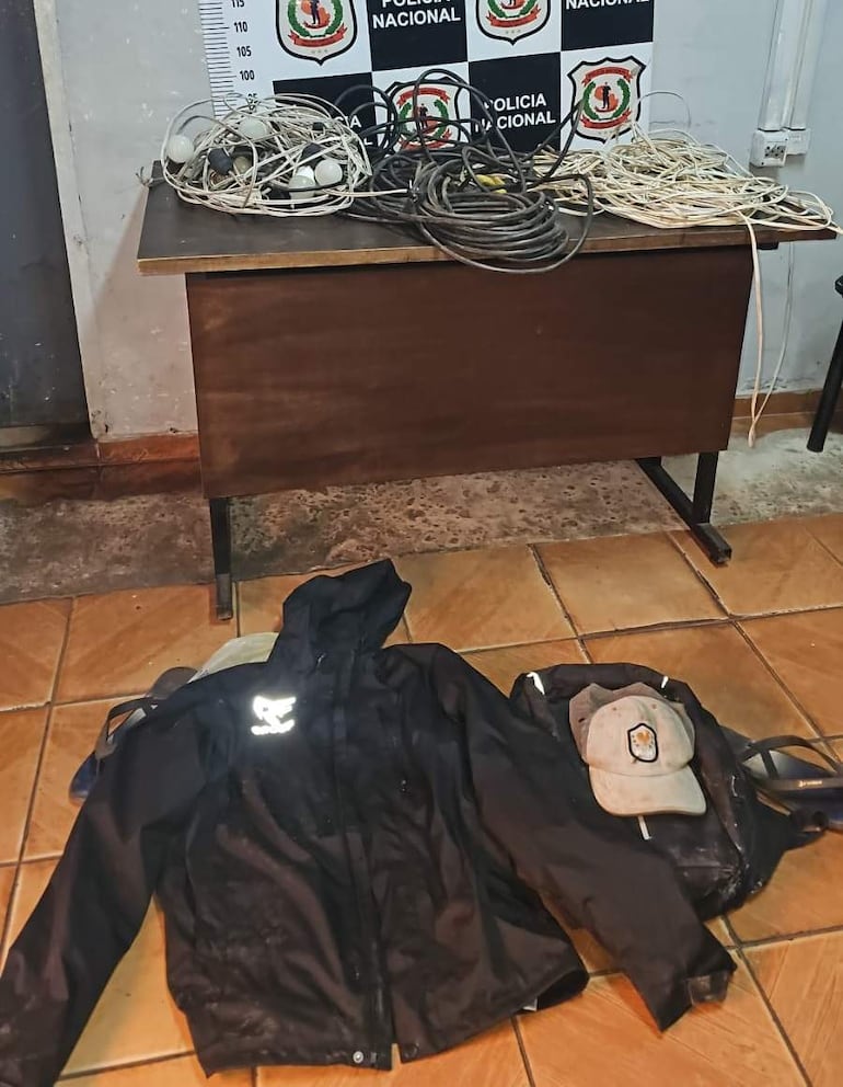 Escritorio de madera con rollos de cable, chaqueta negra y gorra, en un entorno policial.