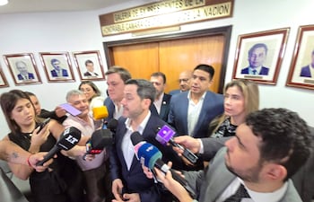 Raúl Latorre en el centro sosteniendo un teléfono, rodeado de personas en un ambiente formal, algunos con micrófonos.