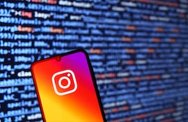 Primer plano de un teléfono móvil con la app de Instagram, rodeado de códigos en tonos azules y naranjas.