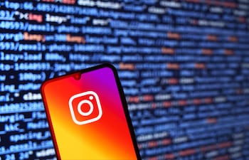 Primer plano de un teléfono móvil con la app de Instagram, rodeado de códigos en tonos azules y naranjas.