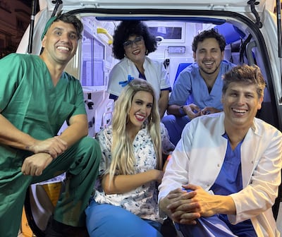 Cinco personas sonrientes en ambulancia, con atuendos médicos y decorativos, destacando un ambiente festivo y de camaradería.