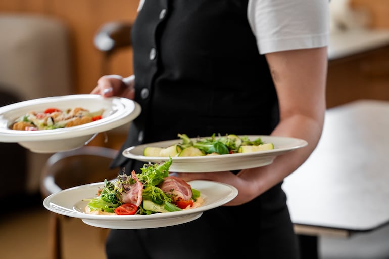 El mozo de un restaurante acerca platos de ensalada a sus comensales en un restaurante.