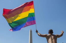 Un hombre flamea una bandera con el arcoiris frente al obelisco de Washington, en Washington DC, en 2017.