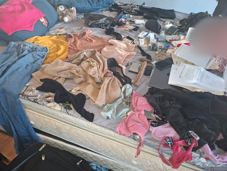 Espacio interior desordenado con ropa variada, documentos y objetos personales esparcidos, sin personas visibles.