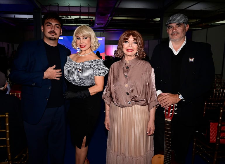Alda Cardozo en vestido negro sonríe, mientras Margarita Franco lleva un vestido beige claro en un evento iluminado.