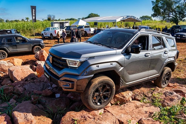 Un SUV gris atraviesa terreno pedregoso mientras personas observan entusiastas la exhibición de vehículos GWM.