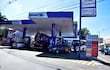 Operario de Petropar abasteciendo un coche en estación de servicio, con precios de combustible visibles en cartel digital en EE.UU y Quinta proyectada