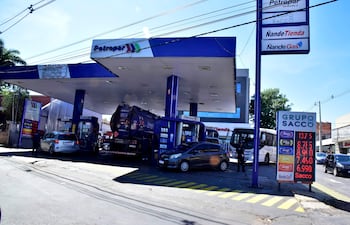 Operario de Petropar abasteciendo un coche en estación de servicio, con precios de combustible visibles en cartel digital en EE.UU y Quinta proyectada