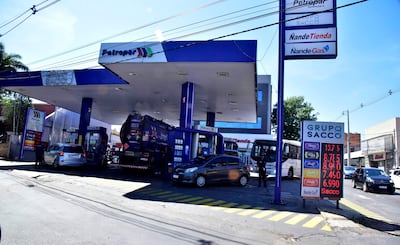 Operario de Petropar abasteciendo un coche en estación de servicio, con precios de combustible visibles en cartel digital en EE.UU y Quinta proyectada