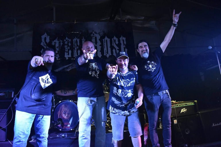 Cuatro músicos en escenario oscuro, vestidos de rockeros, sonríen y hacen el gesto de 'cuernos' tras su presentación.