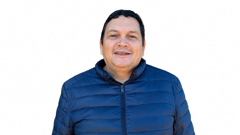 Hombre sonriente con abrigo azul en un fondo blanco, mostrando amabilidad y apertura en su expresión.