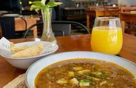 Ambiente acogedor en restaurante con un guiso tradicional y vaso de jugo de naranja sobre la mesa.