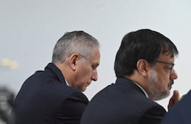 Claudio Lovera y Óscar Boidanich sentados en la sala, ambos en traje oscuro, con expresiones reflexivas.