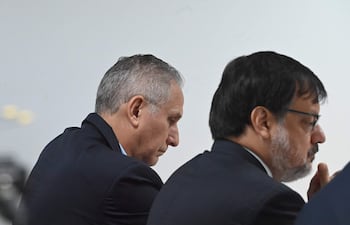 Claudio Lovera y Óscar Boidanich sentados en la sala, ambos en traje oscuro, con expresiones reflexivas.