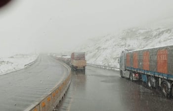 Paisaje nevado con camiones de transporte, carretera resbaladiza y visibilidad limitada por tormenta de nieve.