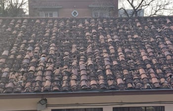 Tejado de cerámica desgastada en edificio afectado por tormenta, con tejas marrón y terracota visibles.