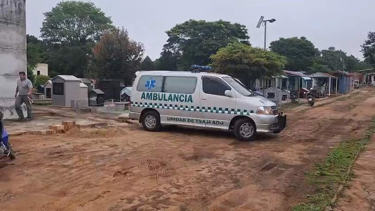 Ambulancia en cementerio con hombre de pie a la izquierda, entorno sombrío y tumbas visibles.