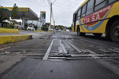 Autobús amarillo de TTA S.A. que pasa por una calle con baches, bajo un cielo nublado y cerca de una estación Petrobras.