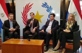Marco Riquelme en el centro con micrófono, acompañado de Javier Giménez, Luis Castiglioni y Liz Cramer, en evento formal con banderas de Paraguay.