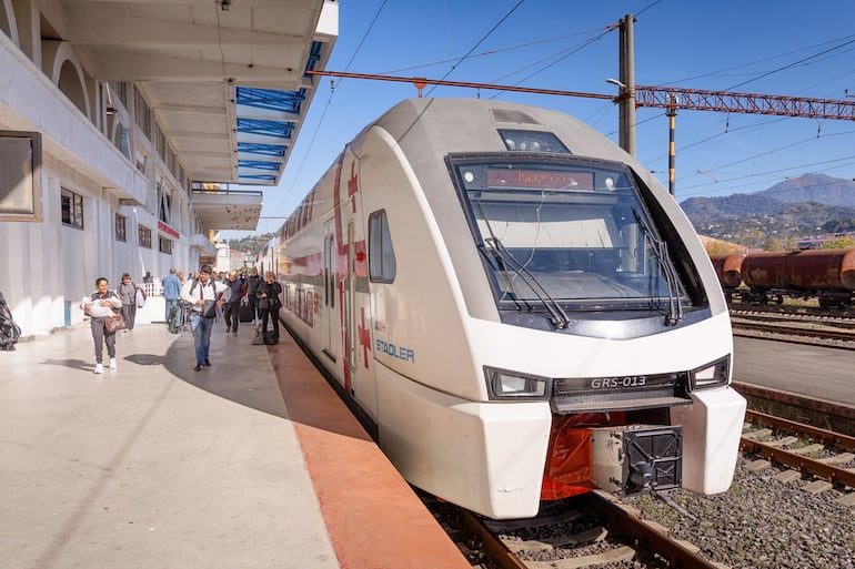 Pasajeros subiendo y bajando de un moderno tren de dos pisos, preparándose para un viaje suburbano en Batumi, Georgia.