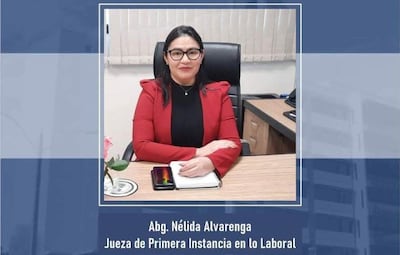 Nélida Alvarenga con abrigo rojo, sentada en su escritorio con brazos cruzados y mirada directa, en ambiente de oficina.