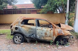 Automóvil quemado y oxidado en terreno descuidado, rodeado de vegetación, sin personas presentes.