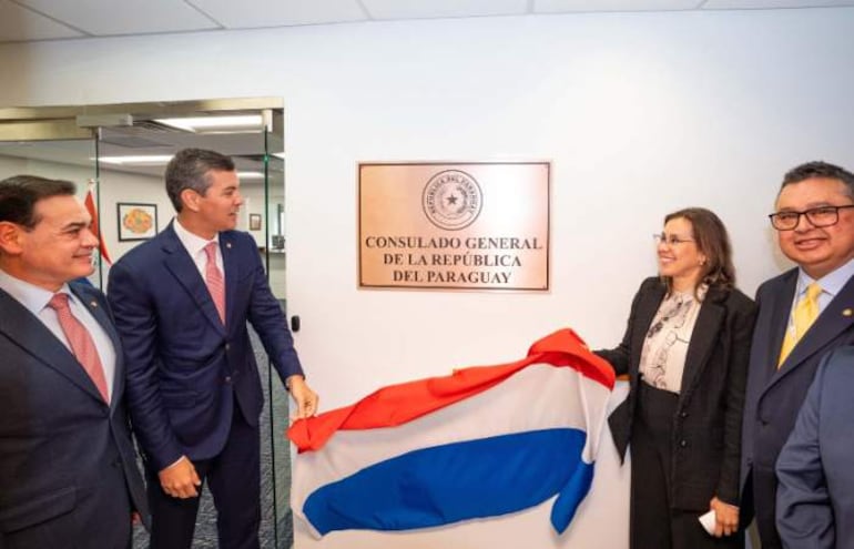Santiago Peña y Rubén Ramírez Lezcano sonríen en la ceremonia, con banderas y documentos, en el consulado paraguayo.