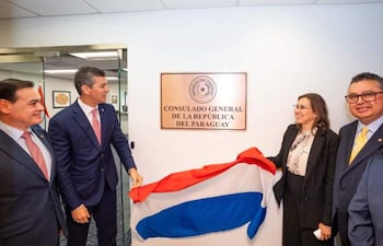 Santiago Peña y Rubén Ramírez Lezcano sonríen en la ceremonia, con banderas y documentos, en el consulado paraguayo.