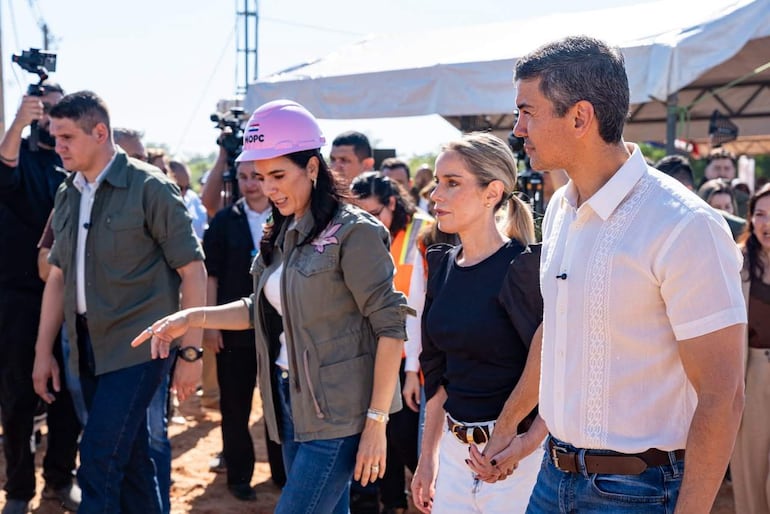 Leticia Ocampos en casco rosa, Santiago Peña en camisa blanca y Claudia Centurión en blusa negra, caminando en un ambiente de construcción.