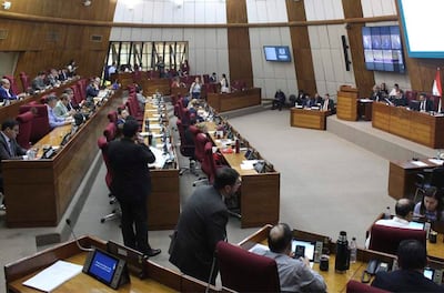 Varios diputados en el recinto legislativo escuchan con atención, con computadoras y pantallas mostrando información sobre la sesión.