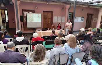 Grupo de personas sentadas en un evento, un hombre y una mujer en panel, mujer con bufanda roja, ambiente formal y de atención.