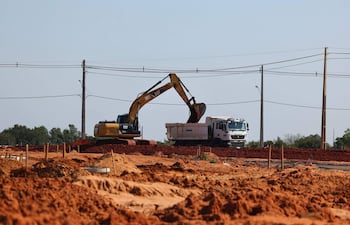 Excavadora amarilla CAT carga material en un camión blanco TIMBO en un terreno de construcción sin trabajadores visibles.