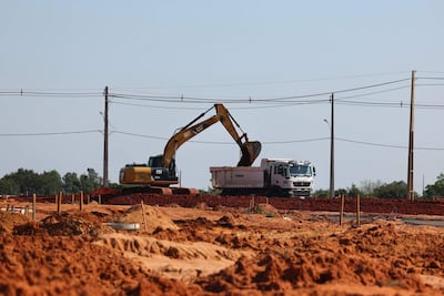 Excavadora amarilla CAT carga material en un camión blanco TIMBO en un terreno de construcción sin trabajadores visibles.