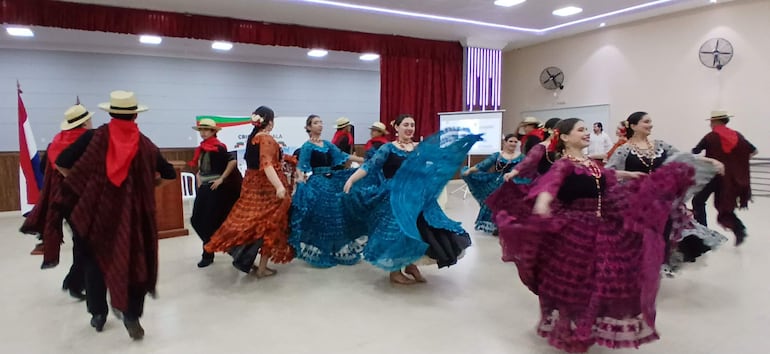Bailarines en trajes coloridos, predominando el azul y púrpura, durante una danza festiva en un ambiente sencillo y decorado.