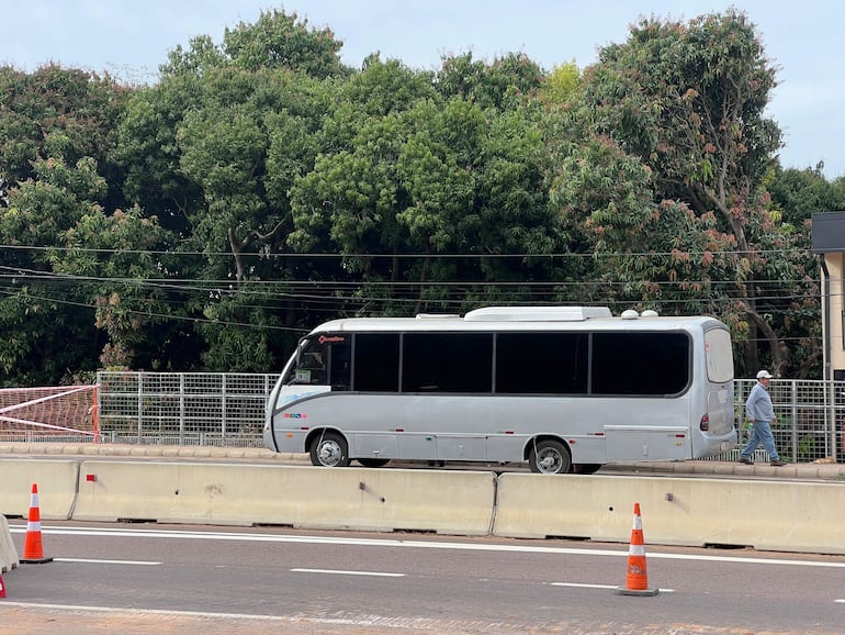 Persona con atuendo claro camina en la acera mientras un autobús plateado circula en un entorno urbano nublado.