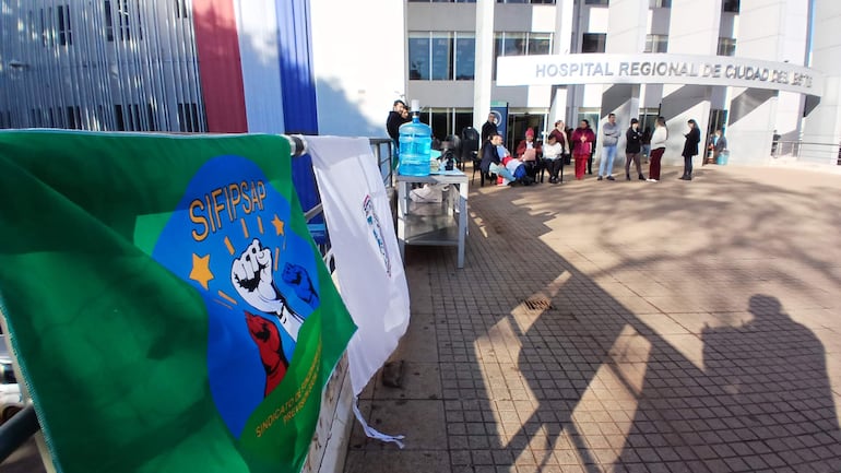 Grupo de personas con bandera del SIFIPSAP, algunos sentados y otros de pie, en un ambiente exterior bien iluminado.