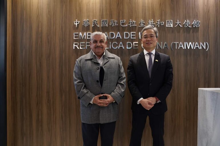 Iván Yueh-Jung Lee, en traje oscuro, y Fretes, en abrigo claro, posan sonrientes frente al letrero de la Embajada de Taiwán.